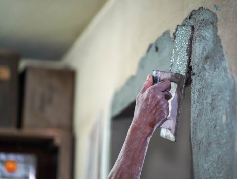 Closeup hands of builder holding mortar pan and plastering walls with cement in construction site.