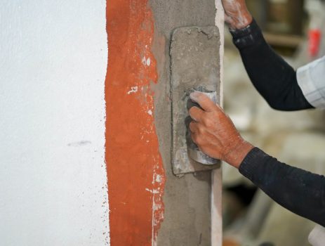 Closeup hands of builder holding mortar pan and plastering walls with cement in construction site.